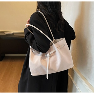 Detail view of beige textured leather tote bag with needle buckle on a shoulder strap