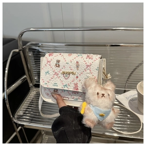 Detail of white textured shoulder bag featuring floral bear prints and cute plush charm