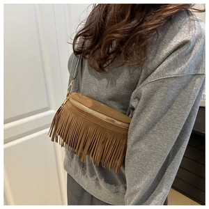 Brown suede crossbody bag with long tassels and zip top closure worn on a gray hoodie