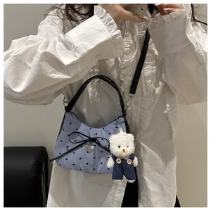 Detail of blue striped canvas handbag with black bow, heart patterns and plush bear charm