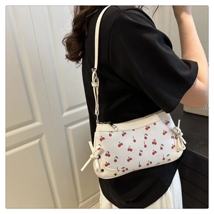 Close-up of a white shoulder bag with cherry prints, rivets and ribbon bow details