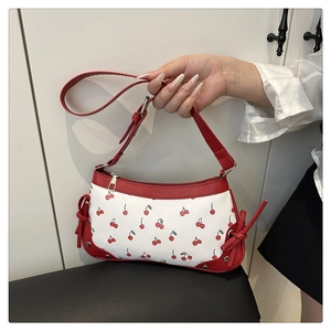 Detail of red cherry print and side knot decoration on a stylish white underarm bag