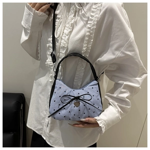 Détail du sac à main rayé avec nœud noir et pendentif cœur sur une blouse blanche