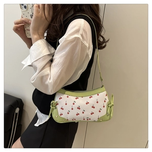 Detail of white baguette bag with green trim and red cherry floral print on bottom