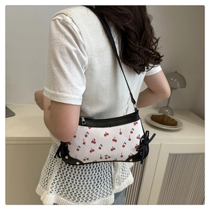Detail of white shoulder bag with red cherry print and black bow charm worn by model