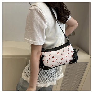 Detail of cherry print shoulder bag with black bow accents and metal hardware on model