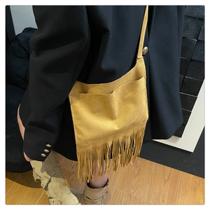 Détail d'un sac à bandoulière en daim jaune gingembre avec de longues franges sur un blazer