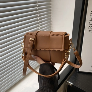 Brown woven crossbody bag with wavy edges and adjustable leather strap in natural light