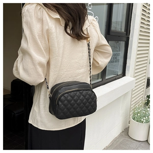 Rear view of model wearing a black quilted crossbody bag with golden chain and dual zippers
