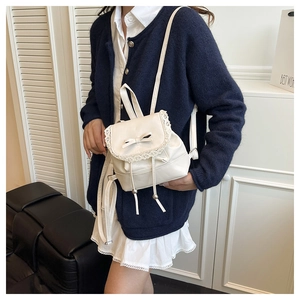 Detail of cream mini bucket bag featuring lace trim, bow accents, and drawstring closure