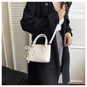 Detail view of cream-colored lychee leather bucket bag with pearl lace bow decoration
