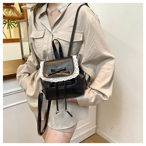 Detail of a mini black leather backpack with white lace trim and a bow detail