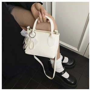 White leather handbag with pearl charm and lace bow detail shown in lifestyle view