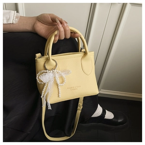 Detail of yellow pebbled leather handbag with pearl charm and lace bow decoration