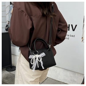 Detail view of black faux leather bucket bag with white lace bow and pearl chain charm