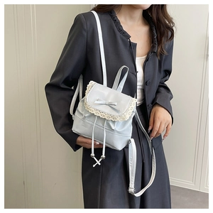Close-up of light blue PU leather mini backpack with lace trim and bow on grey blazer