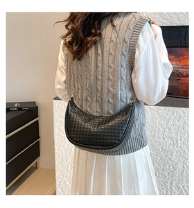 Détail du sac croissant tressé noir avec une chaîne dorée élégante porté par le modèle