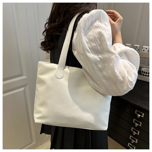 Detail view of a minimalist white tote bag with long handles shown on model shoulder
