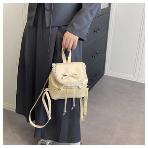 Detail of a beige ballet-style bucket bag with lace trim and leather bow detail