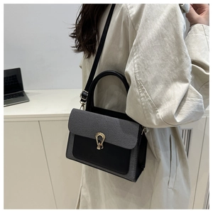 Close-up of stylish grey herringbone crossbody bag with golden horseshoe clasp in office setting