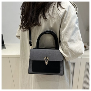 Detail of a black suede and striped handbag with a horseshoe buckle shown on a model