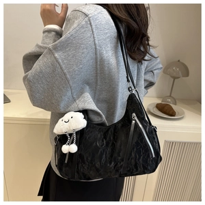 Detail of black pleated shoulder bag with white fluffy cloud charm on a model
