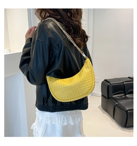 Detail of yellow woven leather crescent bag with gold chain strap on shoulder