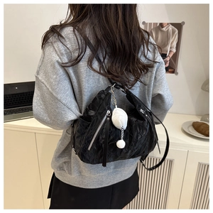 Detail of black pleated texture shoulder bag with a white fluffy ball charm pendant