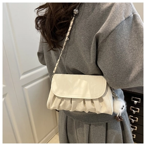 Detail of cream white pleated shoulder bag with chain strap and fuzzy pom pom charm