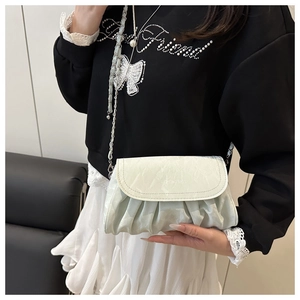 Detail of mint green pleated crossbody bag with silver chain strap on model outfit