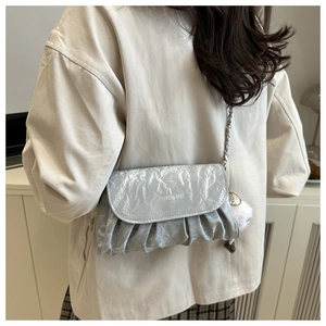 Silver pleated shoulder bag with metal chain strap and white pompom detail shown on model