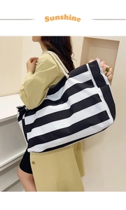 Large striped canvas tote bag with white rope handles worn by a model in a modern style