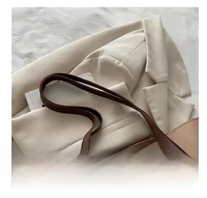 Dettaglio della borsa tote in pelle marrone con spalline sottili su blazer beige e libri