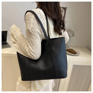 Borsa tote nera minimalista indossata a spalla con manici lunghi e finitura opaca