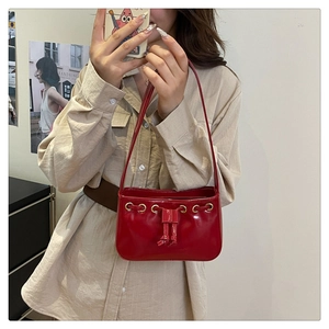 Close-up of a glossy red patent leather shoulder bag featuring golden eyelets and a bow detail