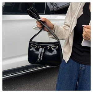 Detail of black patent leather shoulder bag with gold eyelets and drawstring closure