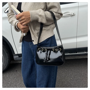 Street style view of a black glossy patent leather shoulder bag with gold metal eyelets