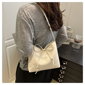 Detail of creamy white leather shoulder bag with decorative bow and brand metal logo