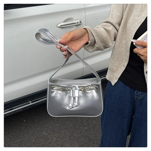 Chic silver metallic handbag featuring gold eyelets and drawstring detail held by a model
