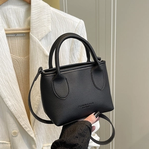 Black lychee pattern bucket bag with handles and shoulder strap held by hand