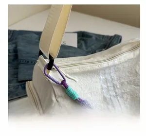 Close-up of white textured crossbody bag featuring a purple woven rope keychain detail