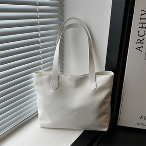 Minimalist white nylon tote bag with long straps shown in a modern sunlit interior