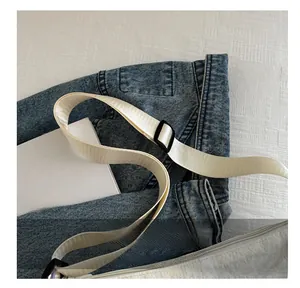 Detail of adjustable off-white nylon strap and blue denim fabric of a shoulder bag
