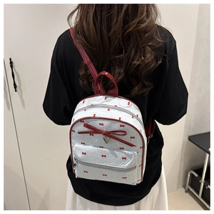 Rear view of a model wearing a mini white backpack with red bow prints and shiny straps