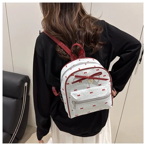 Close-up of a white backpack featuring red bow prints and a 3D decorative bow pendant