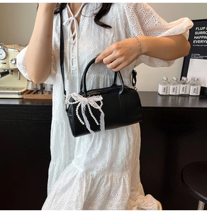 Détail d'un sac Boston noir avec dentelle blanche et nœud orné de perles fines