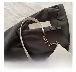 Dettaglio borsa a mezzaluna bianca con emblema W dorato su blazer grigio scuro