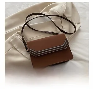 Detail of a brown patchwork square crossbody bag with V-shaped geometric lines and gold hardware