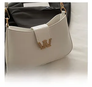 Dettaglio borsa a mezzaluna bianca con logo W dorato e tracolla a catena su blazer nero