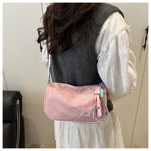 Detail of pink nylon crossbody bag with heart embroidery and colorful woven charm strap